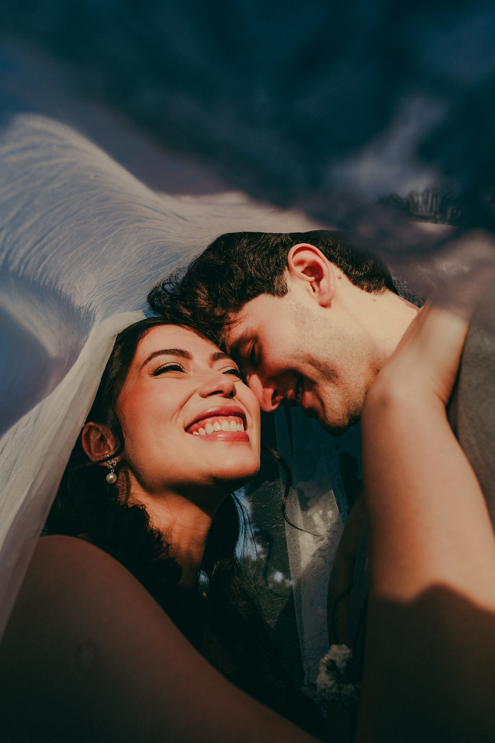 A laughing bride with her partner beneath the veil